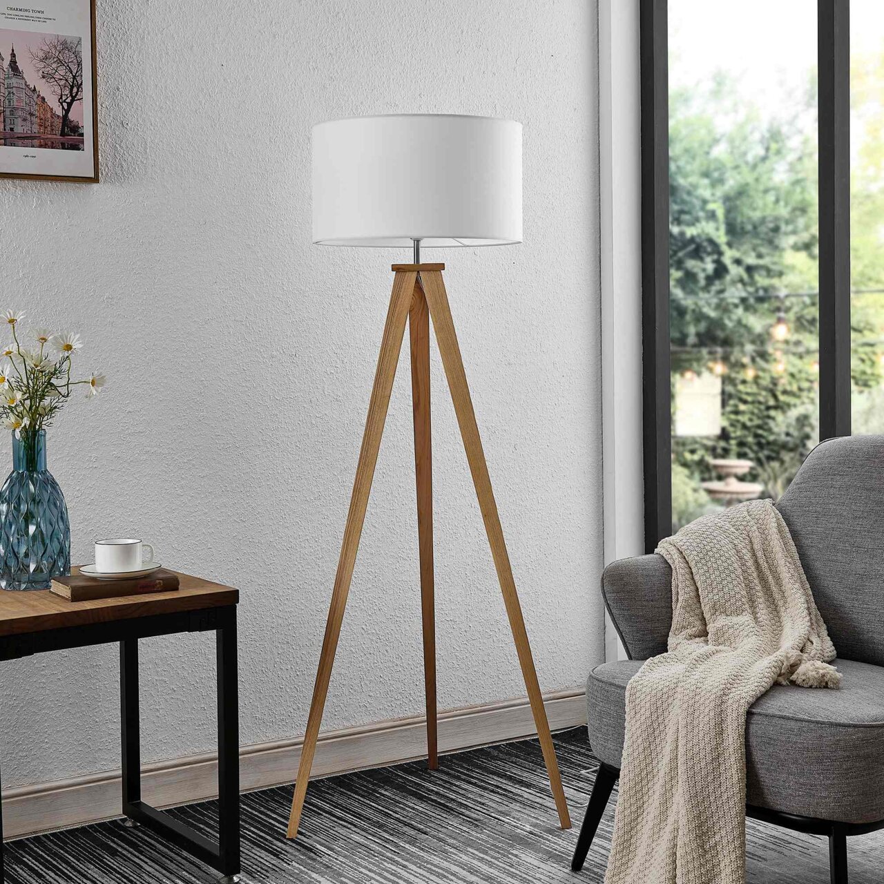 Moderne Stehleuchte mit dreibeinigem Holzgestell und weißem Lampenschirm, seitliche Perspektive im Wohnzimmer.