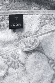 Close-up van een grijze saunadoek met een zwart Joop!-label.
