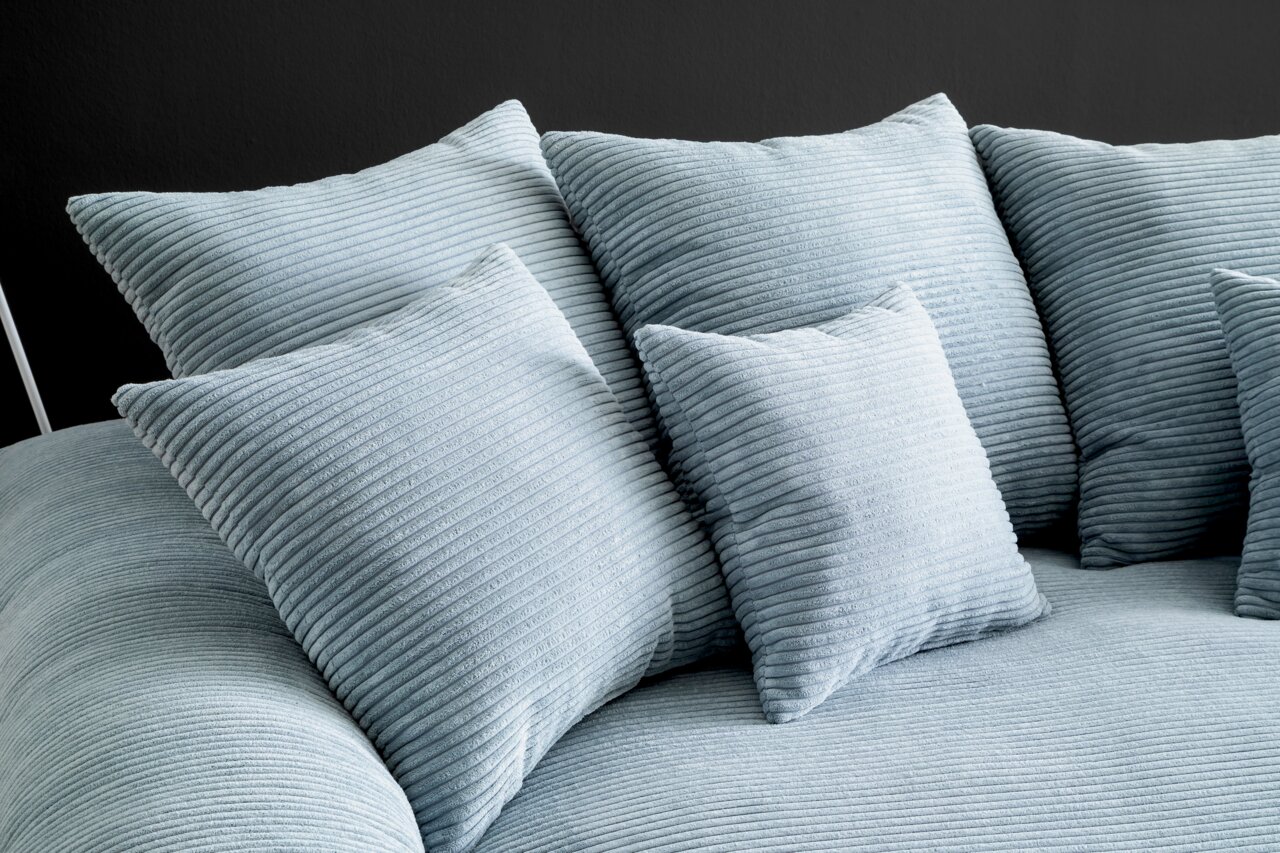 Nahaufnahme eines Big-Sofas mit mehreren großen, gerippten Kissen in hellblauer Farbe, seitliche Perspektive.