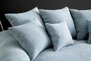 Nahaufnahme eines Big-Sofas mit mehreren großen, gerippten Kissen in hellblauer Farbe, seitliche Perspektive.