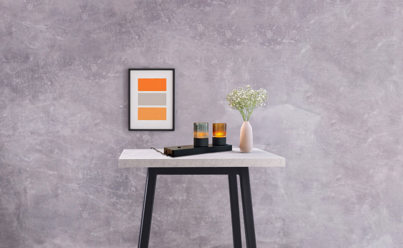 Moderne Akku-Windlicht-Tischleuchte auf einem Tisch, frontal fotografiert, neben einer Vase mit Blumen und einem gerahmten Bild an der Wand.