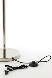 Nahaufnahme der Basis einer Stehleuchte mit glänzendem Metallfuß und schwarzem Kabel mit Fußschalter.