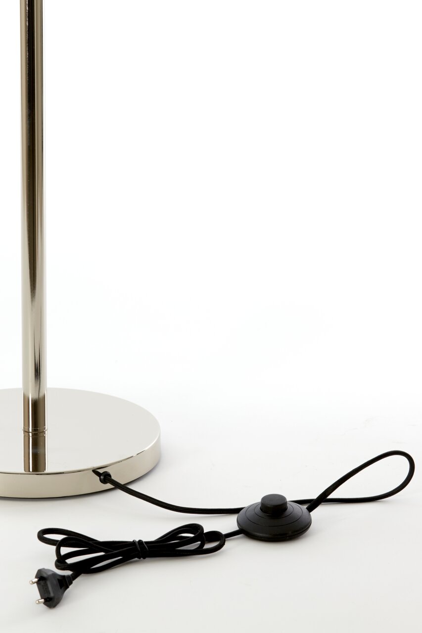 Close-up van de voet van een staande lamp met een glanzende metalen voet en een zwarte kabel met voetschakelaar.