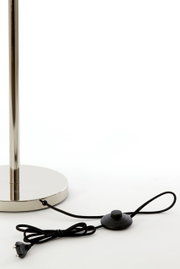 Close-up van de voet van een staande lamp met een glanzende metalen voet en een zwarte kabel met voetschakelaar.
