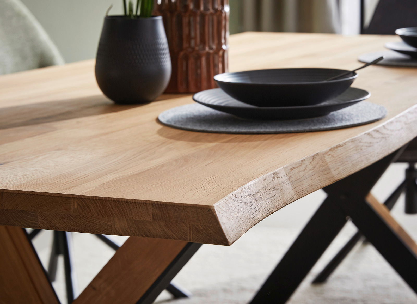Nahaufnahme eines Esstisches aus Holz mit schwarzem Geschirr und Dekoration, seitliche Perspektive.