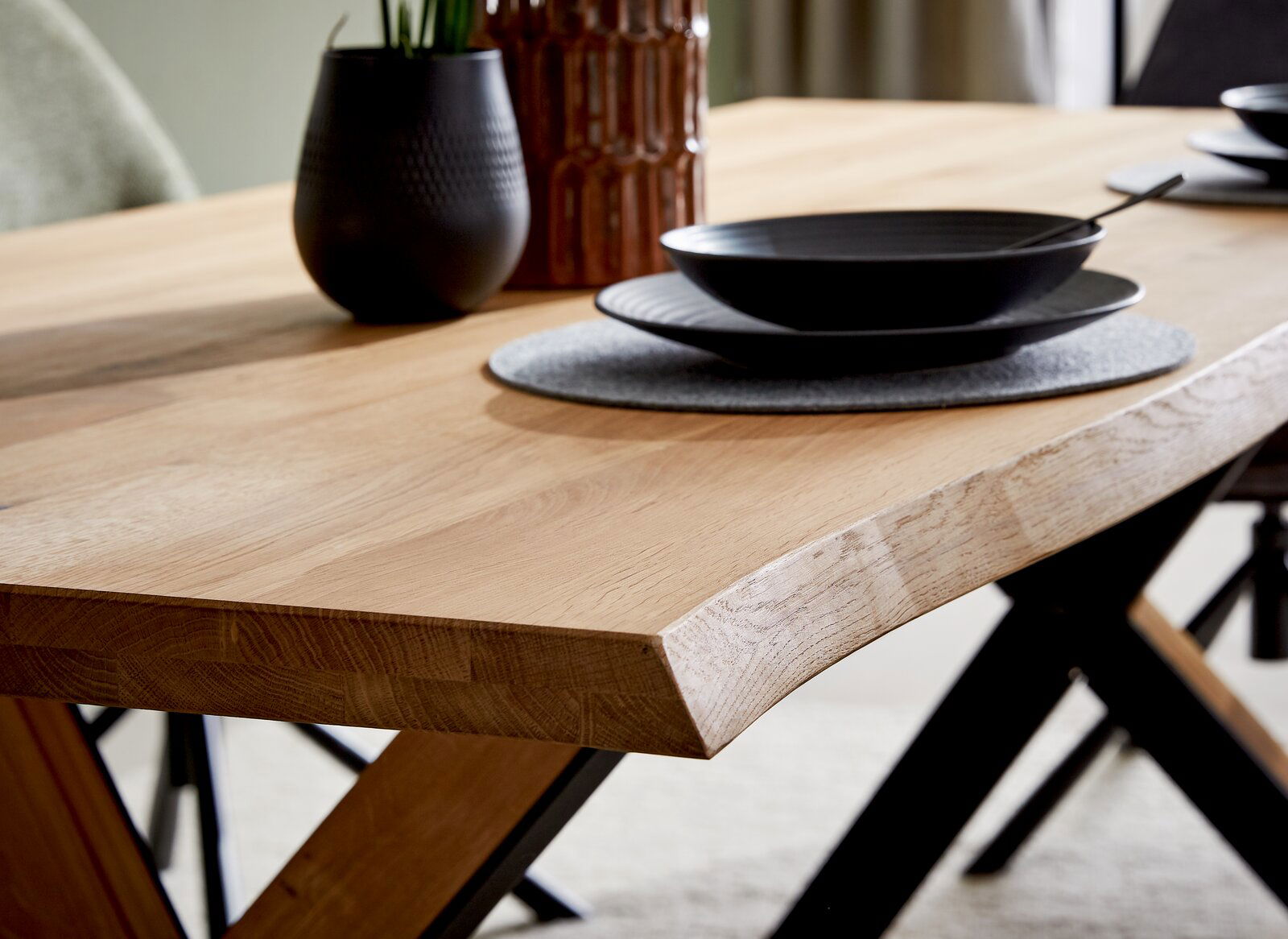 Nahaufnahme eines Esstisches aus Holz mit schwarzem Geschirr und Dekoration, seitliche Perspektive.
