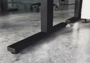 Nahaufnahme der stabilen, schwarzen Metallbeine eines höhenverstellbaren E-Schreibtisches auf einem modernen Betonboden.