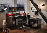 Moderner Gaming-Schreibtisch mit zwei Monitoren, beleuchtetem PC-Gehäuse und ergonomischem Stuhl in einem stilvollen Raum mit Stadtblick, aus seitlicher Perspektive.