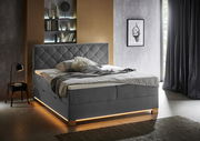 Modernes Boxspringbett in einem stilvollen Schlafzimmer, seitliche Perspektive, mit grauem Kopfteil und integrierter Beleuchtung.