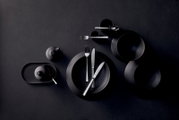 Schwarzes, mattes Geschirr- und Besteck-Set mit Tellern, Schalen, Tassen und Messer/Gabel/Löffel auf dunklem Hintergrund, fotografiert aus der Vogelperspektive (Top-Down).