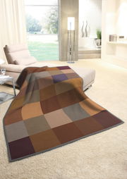 Gemütliche Wohndecke in warmen Erdtönen mit Karomuster, drapiert über einem Sofa in einem modernen Wohnzimmer mit Blick auf den Garten.