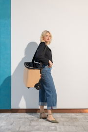 Frau in seitlicher Perspektive mit einem beigen carrycruiser auf Rollen, der über der Schulter getragen wird.