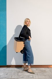 Frau in seitlicher Perspektive mit einem beigen carrycruiser auf Rollen, der über der Schulter getragen wird.