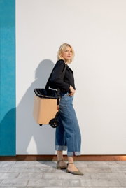 Vrouw in zijaanzicht met een beige carrycruiser op wieltjes, die over de schouder wordt gedragen.
