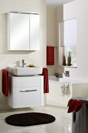 Moderner Spiegelschrank im Badezimmer, frontal betrachtet, über einem Waschbecken mit roten Handtüchern.