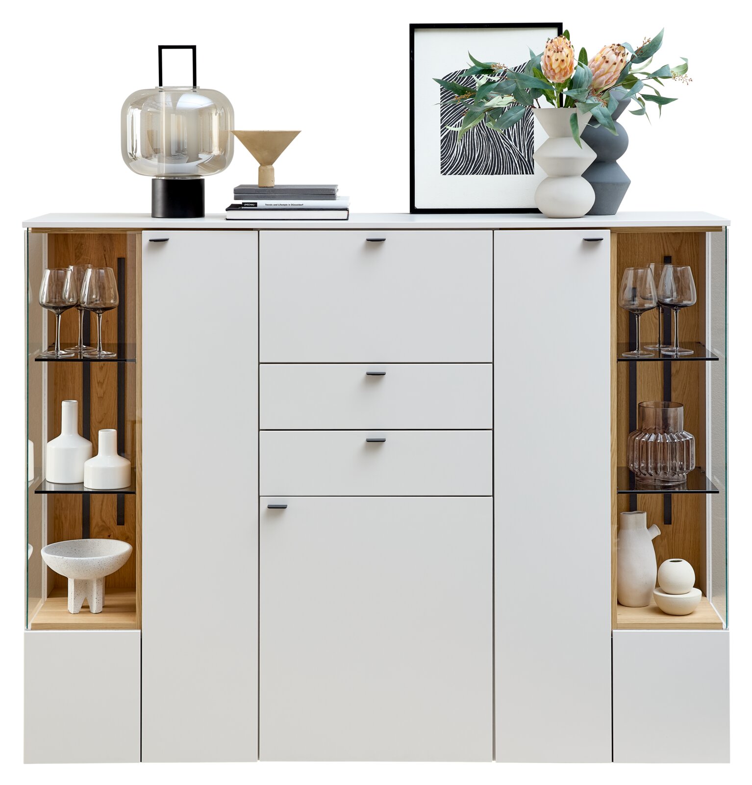 Frontale Ansicht eines modernen Highboards mit weißen Türen und Schubladen, flankiert von Glasvitrinen mit dekorativen Objekten.