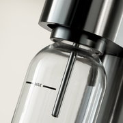 Nahaufnahme einer Wasserflasche in einem modernen Wassersprudler aus Edelstahl, seitliche Perspektive.