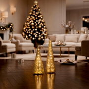 Zwei unterschiedlich hohe, kegelförmige LED-Dekoleuchten in goldener Glasoptik, frontal auf einem Holzboden in einem festlich geschmückten Wohnzimmer präsentiert