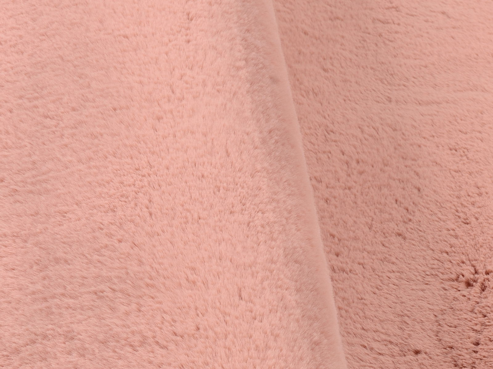 Nahaufnahme eines rosafarbenen Fellteppichs in weicher Textur, schräg von der Seite fotografiert.
