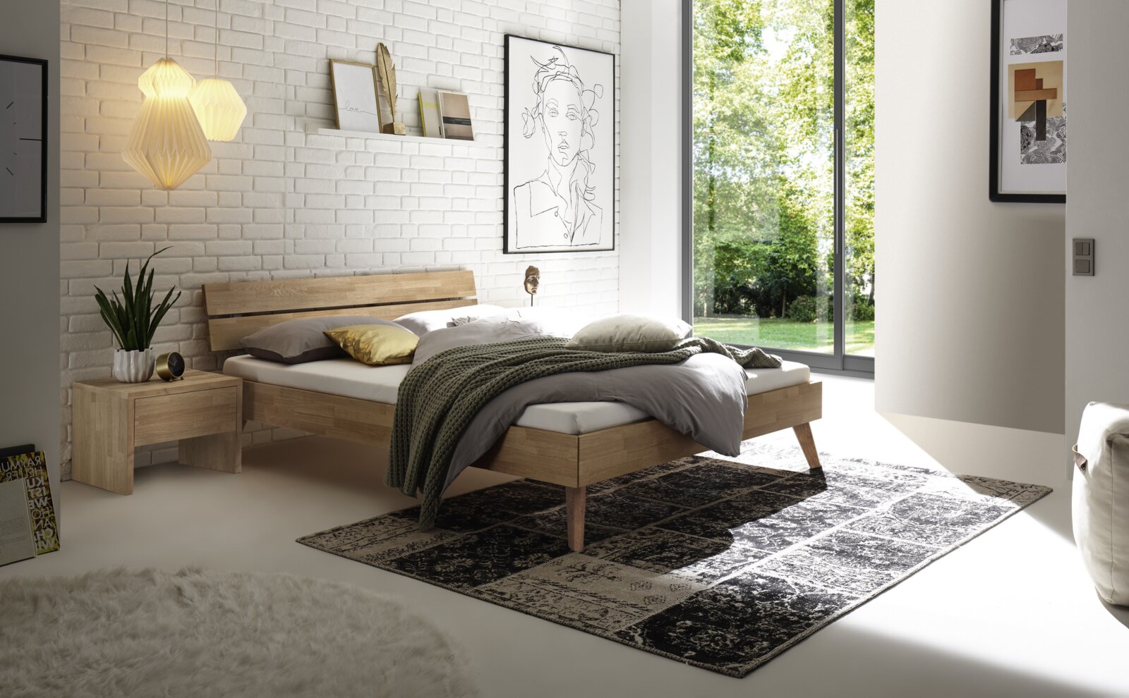 Modernes Schlafzimmer mit einem Kopfteil aus Holz und Metall, seitliche Perspektive. Das Bett ist mit neutralen Farben dekoriert und steht vor einer weißen Ziegelwand mit Kunstwerken. Große Fenster lassen viel Tageslicht herein.