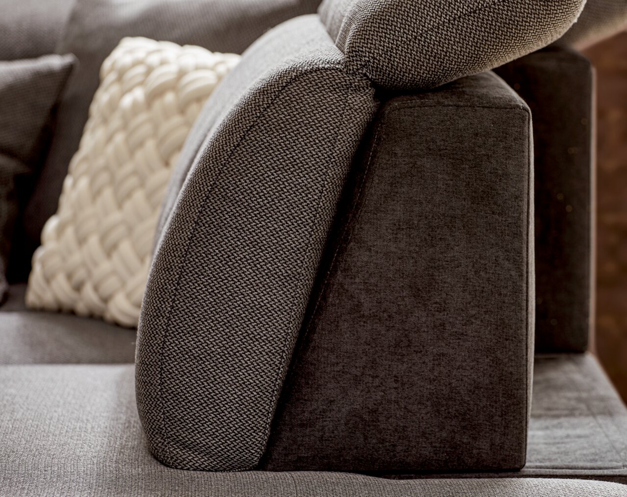 Seitenansicht einer modernen, grauen Rundecke mit verstellbarer Kopfstütze und dekorativem Kissen.