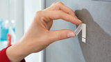 Nahaufnahme einer Hand, die einen tesa Powerstrip Waterproof an einer Wand anbringt.