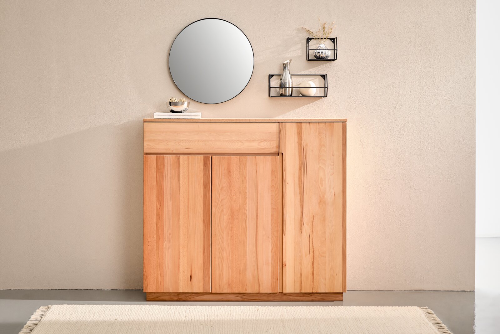 Linea Natura XL-Schuhschrank LINEA Frontale Ansicht einer modernen, hellen Holz-Kommode/Sideboard mit zwei Türen und einer oberen Schublade, dekoriert mit rundem Wandspiegel und zwei schwarzen Wandregalen vor beiger Wand.