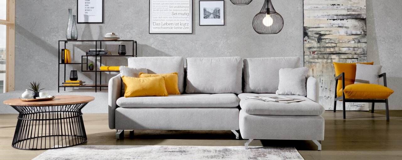 Graue Rundecke mit gelben Kissen in modernem Wohnzimmer, frontal betrachtet.