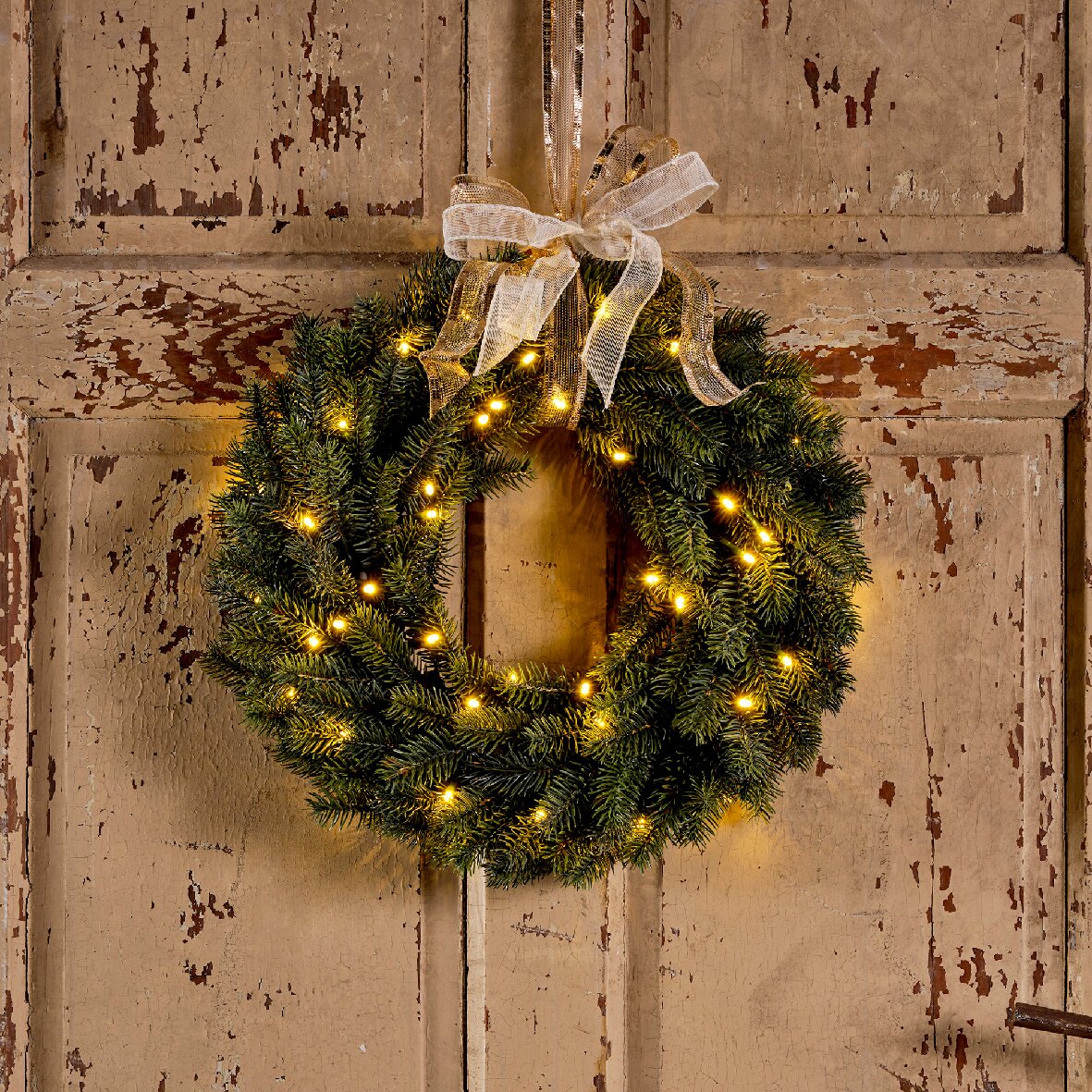 Weihnachtskranz mit Lichtern und Schleife, frontal an einer Holztür aufgehängt