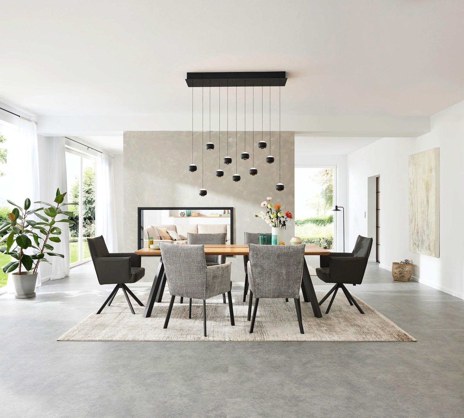 Esszimmer mit modernem Esstisch und Armlehnstühlen, frontal betrachtet. Helle, minimalistische Einrichtung mit großen Fenstern und hängender Beleuchtung.