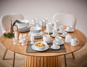 Ein 62-teiliges Kombiservice-Set auf einem runden Holztisch, bestehend aus Tellern, Tassen, Schalen und Eierbechern in schlichtem Weiß. Die Perspektive zeigt das Set von oben, mit zwei Stühlen im Hintergrund.