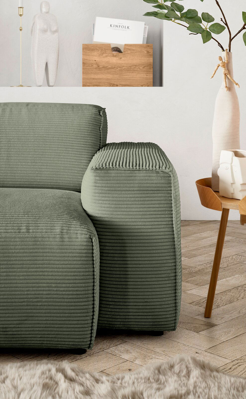 Grüne Rundecke mit geripptem Stoffbezug, seitliche Perspektive, neben einem Holztisch mit Dekorationen.