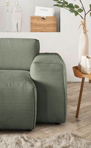 Grüne Rundecke mit geripptem Stoffbezug, seitliche Perspektive, neben einem Holztisch mit Dekorationen.