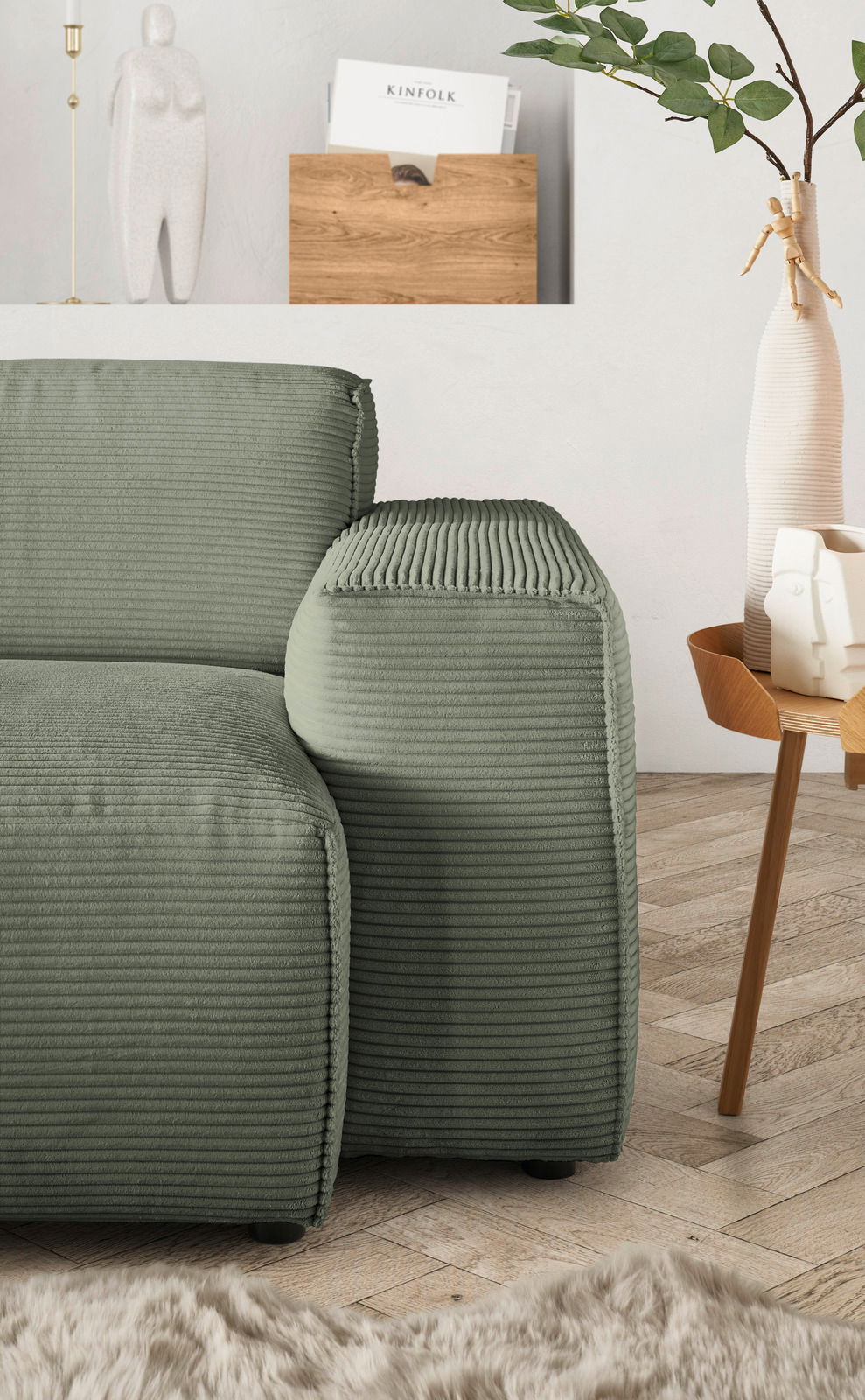Grüne Rundecke mit geripptem Stoffbezug, seitliche Perspektive, neben einem Holztisch mit Dekorationen.