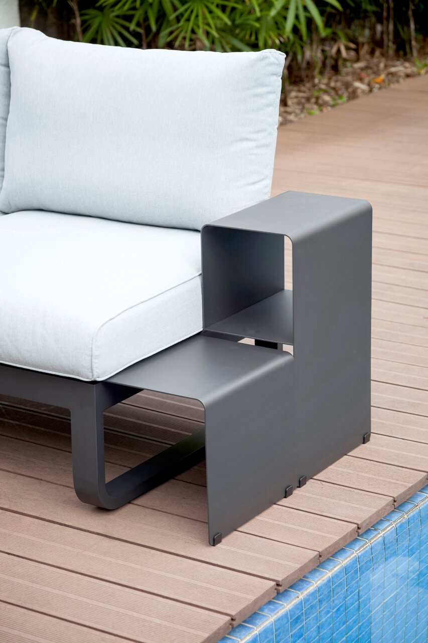 Moderner Lounge Beistelltisch aus Metall in anthrazitgrau, seitliche Perspektive neben einem hellen Outdoor-Sofa, auf einer Holzterrasse am Pool.