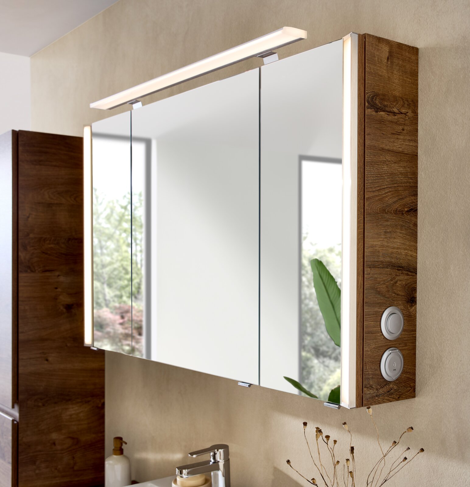 Moderner Badezimmerspiegelschrank mit drei Spiegeltüren, Holzseiten in Eiche-Optik und LED-Aufsatzleuchte sowie seitlicher Bedienung, schräg von vorne rechts aufgenommen