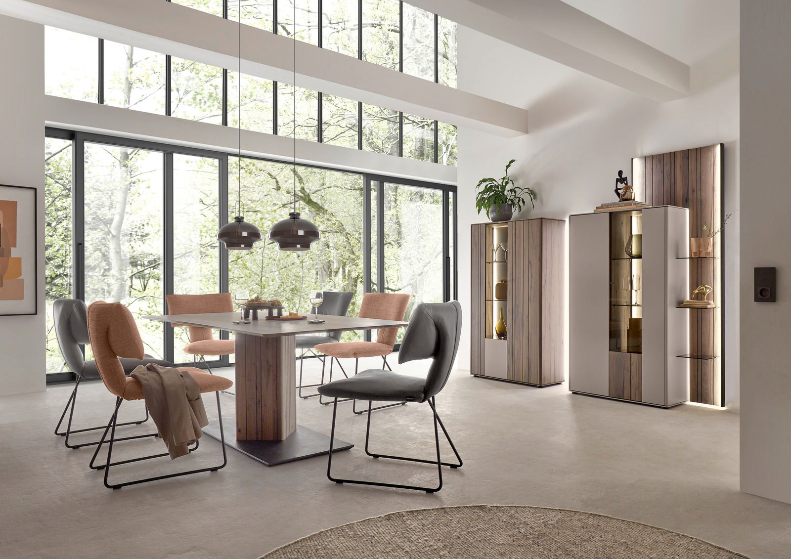 Moderner Esstisch in einem hellen Raum mit großen Fenstern, umgeben von stilvollen Stühlen und dekorativen Schränken, seitliche Perspektive.