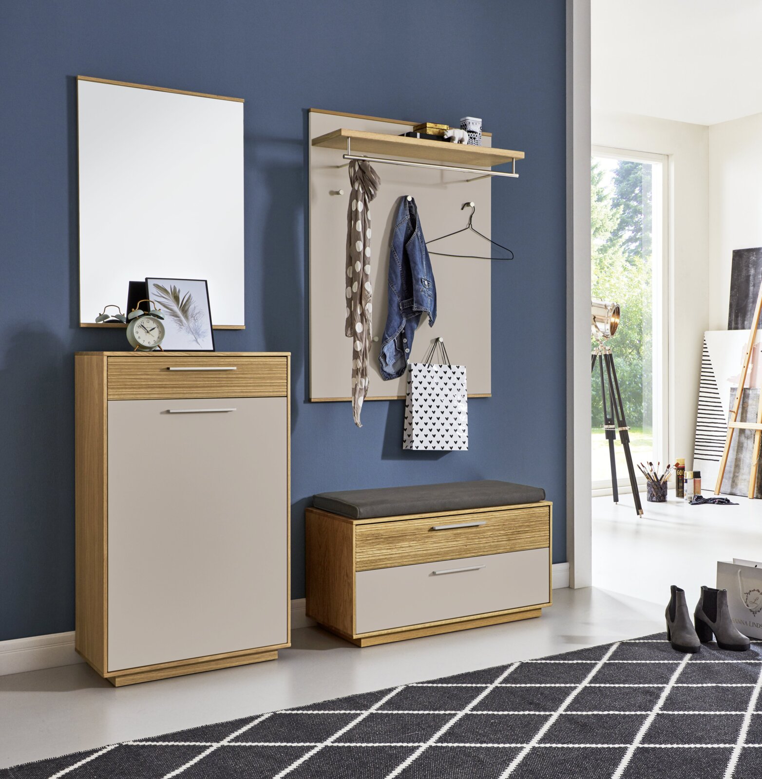 Moderner Garderoben-Set im Flur mit Spiegel, Wandgarderobe mit Hutablage und Kleiderstange sowie Schuhbank und Schrank in Holzoptik mit hellen Fronten, frontal aus leicht seitlicher Perspektive fotografiert