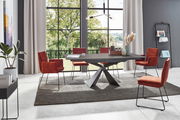 Moderner Esstisch mit schwarzer Tischplatte und X-förmigem Gestell, umgeben von roten Stühlen in einem hellen Raum mit großen Fenstern, seitliche Perspektive.