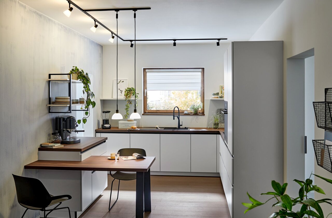 Moderne Küche mit Schienenspot-Beleuchtung an der Decke, Blick von der Seite auf die Arbeitsfläche und den Esstisch.