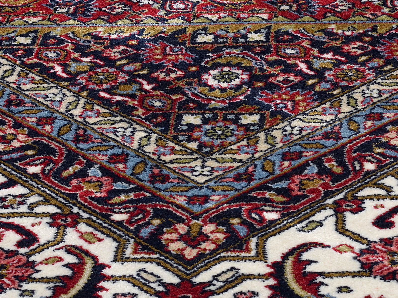 Nahaufnahme eines Orientteppichs mit komplexen Mustern in Rot, Blau, Weiß und Goldtönen, schräg von oben fotografiert.