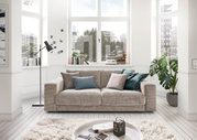 Gemütliches zweisitziges Sofa in einem hellen Wohnzimmer mit großen Fenstern, dekoriert mit Kissen in verschiedenen Farben, aus der Frontalperspektive.
