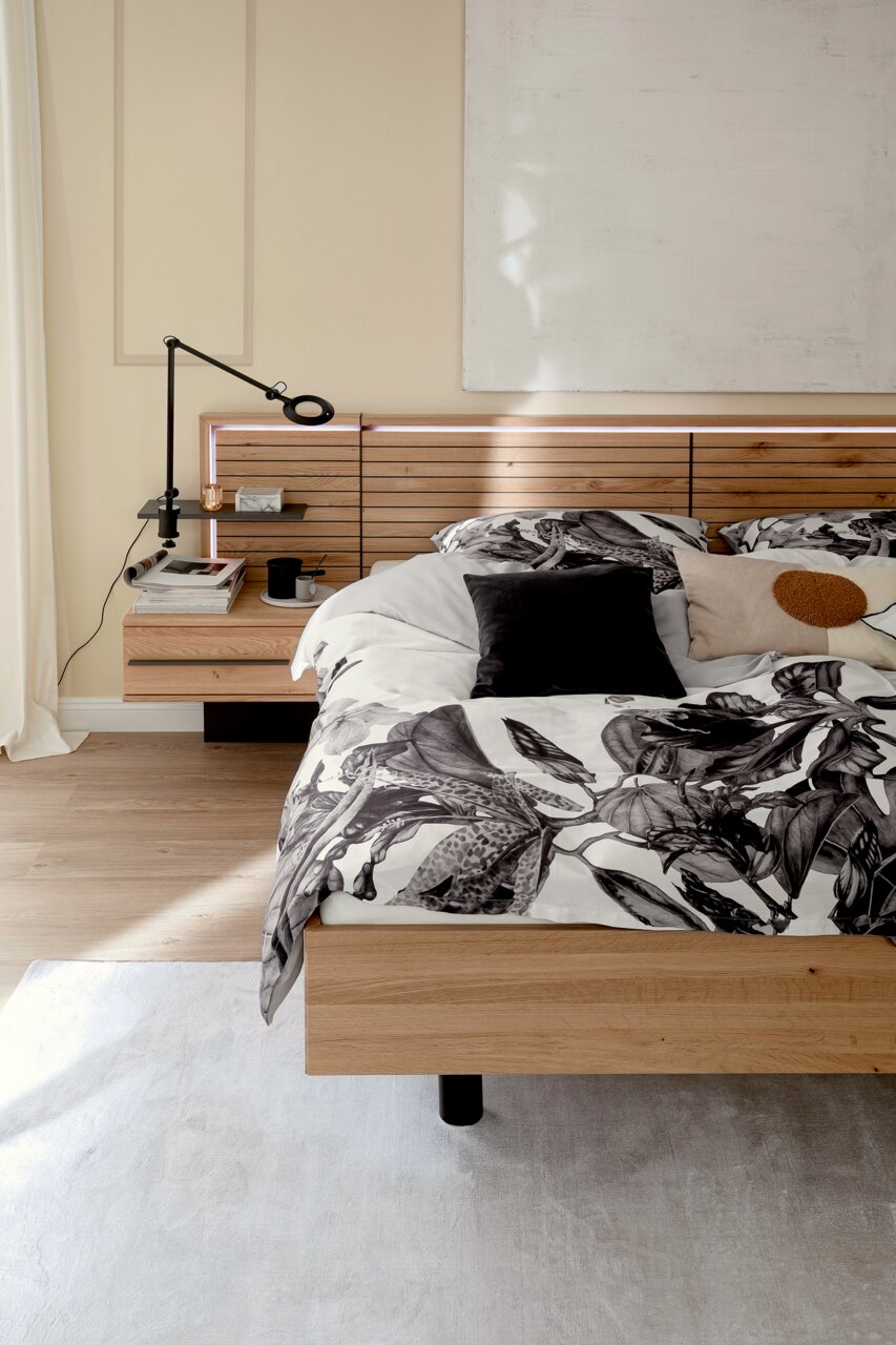 Satin-Bettwäsche AMALIA in einem modernen Schlafzimmer, mit floralem Muster in Schwarz-Weiß, auf einem Holzrahmenbett, seitliche Perspektive.