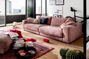 Gemütliches rosa Sofa in einem modernen Wohnzimmer mit großen Fenstern, dekoriert mit Kissen und Decken, seitliche Perspektive.