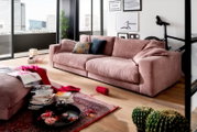 Gezellige roze bank in een moderne woonkamer met grote ramen, versierd met kussens en dekens, zijaanzicht.
