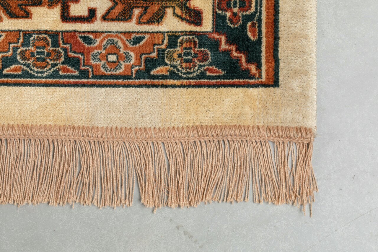 Nahaufnahme eines Teppichs mit Fransen und traditionellem Muster in Rot-, Blau- und Beigetönen, von oben betrachtet.