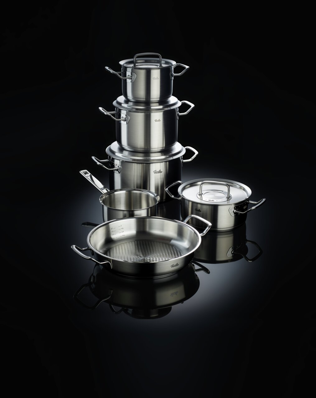Topfset Original-Profi 5-teilig, bestehend aus mehreren Edelstahltöpfen und Pfannen, auf schwarzem Hintergrund, seitliche Perspektive.