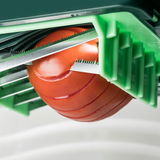 Nahaufnahme eines Nicer Dicer Chef, der eine Tomate in gleichmäßige Scheiben schneidet. Die Perspektive zeigt die scharfen Klingen und die grüne Halterung von der Seite.