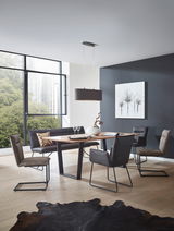 Moderner Essbereich mit einem rechteckigen Holztisch und vier Freischwinger-Stühlen in einem hellen Raum mit großen Fenstern, seitliche Perspektive.