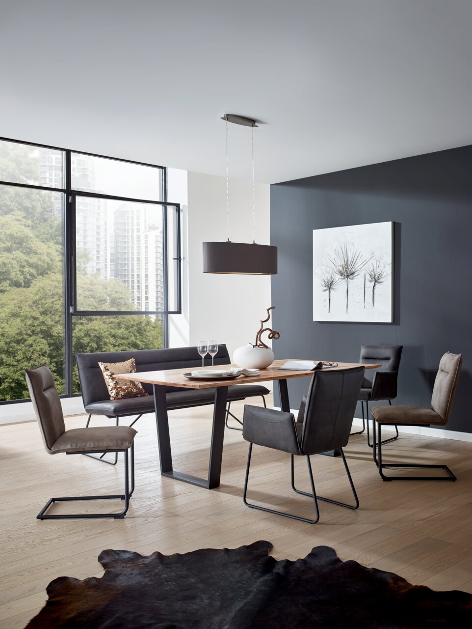 Valnatura Bank SCALA Moderner Essbereich mit einem rechteckigen Holztisch und vier Freischwinger-Stühlen in einem hellen Raum mit großen Fenstern, seitliche Perspektive.